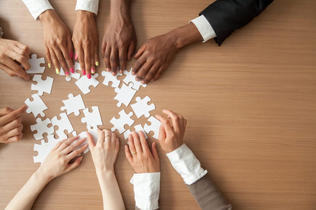 Hands of coworkers putting puzzle pieces together on a table