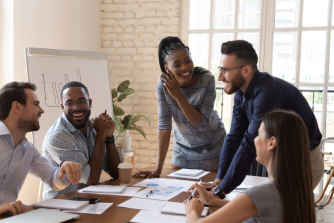 Team members smile and laugh as they gather around a table during a meeting